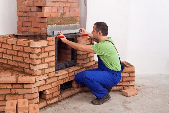 Mason fitting a firebox door into a brick masonry heater