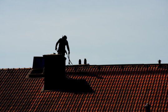 Sweep silhouetted at a chimney above a steep roof